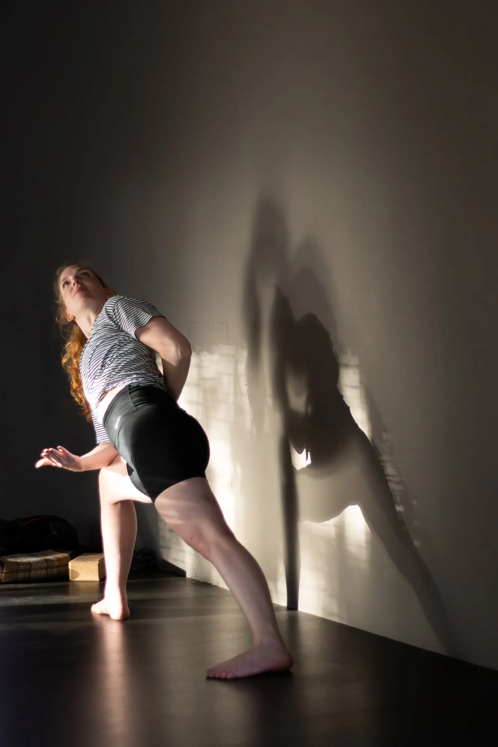 Vrouw in een staande yogahouding met haar schaduw op de muur